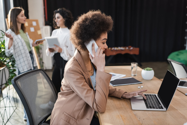 Afrikaans amerikaanse zakenvrouw praten op mobiele telefoon en met behulp van laptop met leeg scherm in het kantoor  - Foto, afbeelding