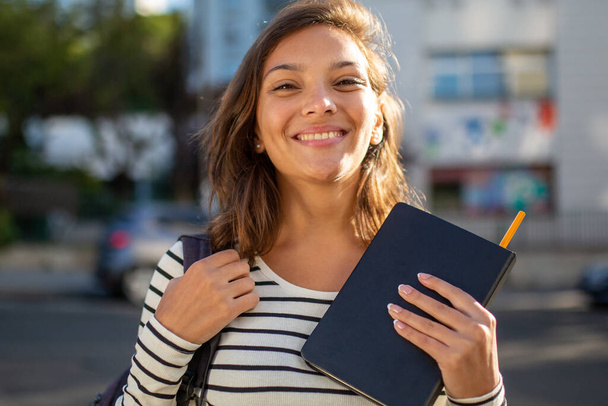 Close up portrait of happy female student with bag and book in city - Valokuva, kuva