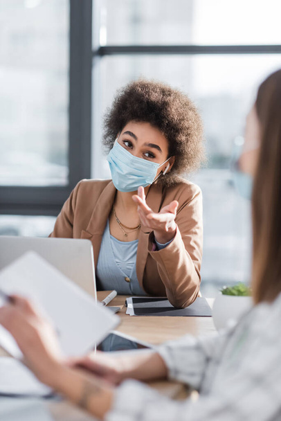 African american businesswoman in medical mask pointing at blurred colleague  - Foto, imagen