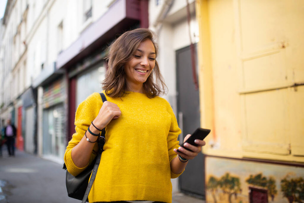 Horizontální portrét šťastné mladé ženy kráčející ve městě s mobilním telefonem - Fotografie, Obrázek