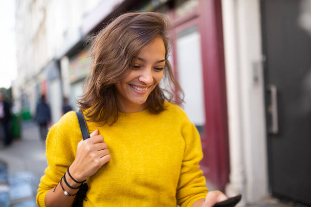 Close up portrait of smiling young woman looking at cellphone in city - Foto, Imagen