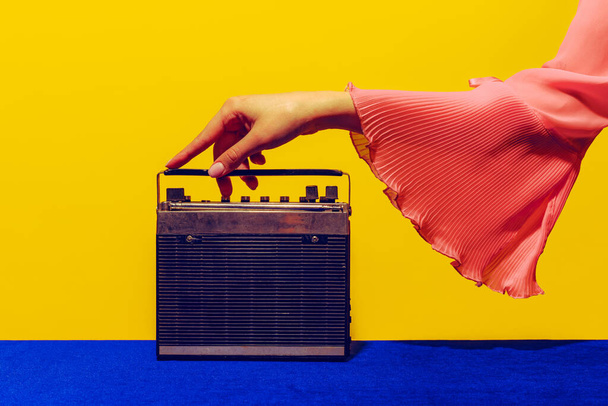 Old radio. Female hand touching radior, wireless isolated on bright blue and yellow background. Vintage, retro fashion style. Pop art photography. - Photo, Image