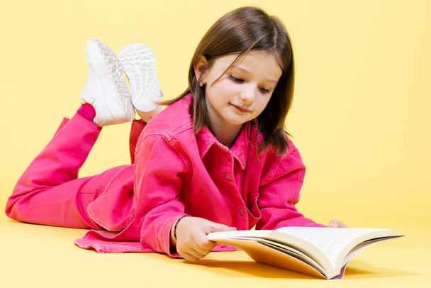 Kleines Mädchen liegt auf gelbem Hintergrund und liest ein Buch. - Foto, Bild