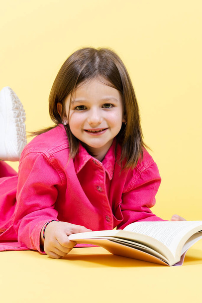 Lächelndes kleines Mädchen, das ein Buch in der Hand hält und direkt in die Kamera schaut. - Foto, Bild