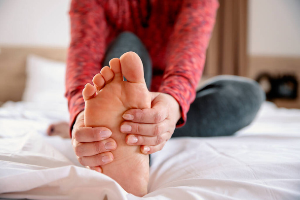 Female massaging bare foot in bed, close up. Stretching leg muscles in the morning - Foto, imagen