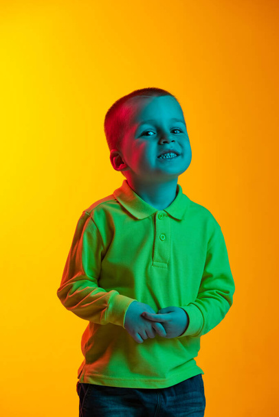 Portrait of cute little boy smiling isolated on yellow studio backgroud in neon light. Concept of child emotions, facial expression, childhood - Photo, Image