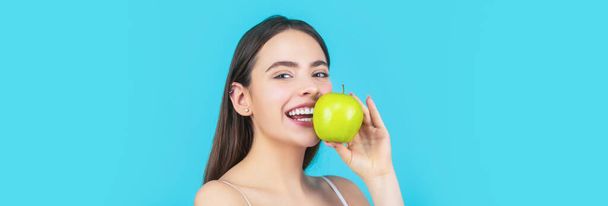 緑のリンゴと若い美しい幸せな笑顔の女性の肖像画。健康的な食事。ストーモロジーの概念。完璧な笑顔を保持リンゴ、青の背景を持つ女性。女性は緑のリンゴを食べる - 写真・画像
