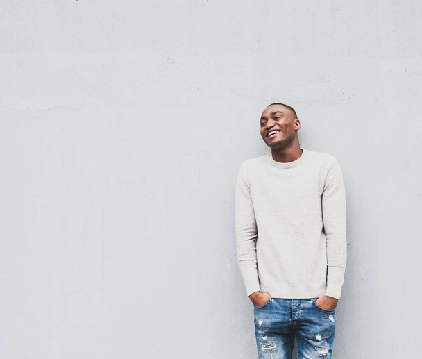 Portrait of happy African american man with hands in pockets by white wall - Photo, image