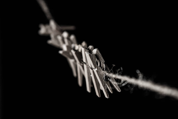 Small wooden clothespins attached to a rope on a black background. Detail close-up - Foto, immagini