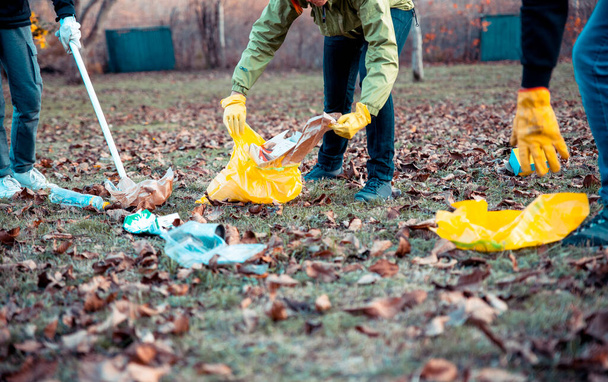 Les gens nettoient et ramassent les ordures à l'extérieur dans le champ du parc. Les bénévoles ramassent les ordures de l'herbe le jour d'automne. Militant écologiste ramassant des ordures dans la nature. Espace de copie - Photo, image