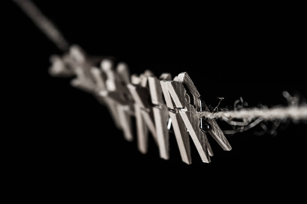 Невеликі дерев'яні прищіпки, прикріплені до мотузки на чорному тлі. Деталі крупним планом
 - Фото, зображення