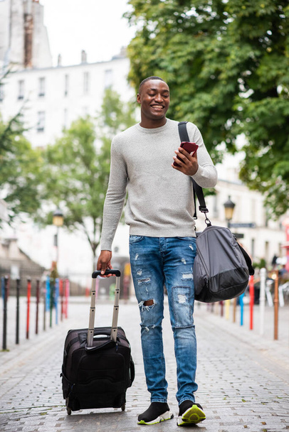 Портрет щасливого африканського мандрівника - американця, який ходить по вулиці з мобільним телефоном і валізою. - Фото, зображення