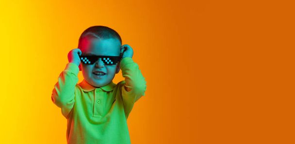 Happy cute little boy, child smiling isolated on yellow studio backgroud in neon light. Concept of child emotions, facial expression, childhood - Photo, image