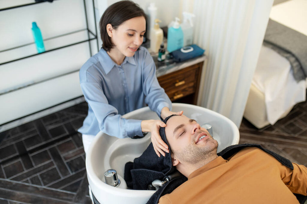 Beautician massaging mans head during hair treatment procedures - Фото, изображение