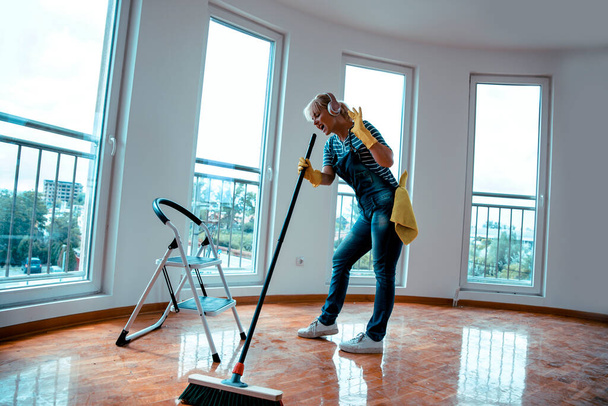 Happy Woman dancing and singing with headset during cleaning new home. Copy space. Cleaning home after party - Fotoğraf, Görsel