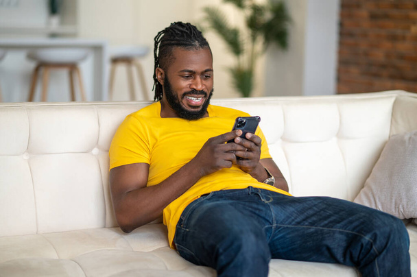 Man sitting on sofa looking at smartphone - Foto, afbeelding