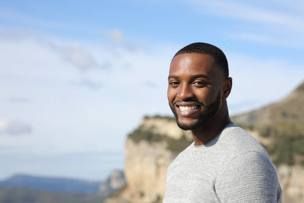 Portrait of a handsome happy man with black skin looking at camera in nature - Foto, Imagen