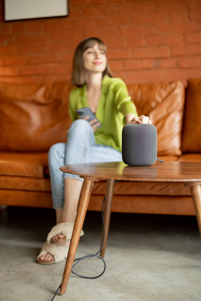 Nő megérinti okos hangszóró, miközben ül a kanapén otthon - Fotó, kép
