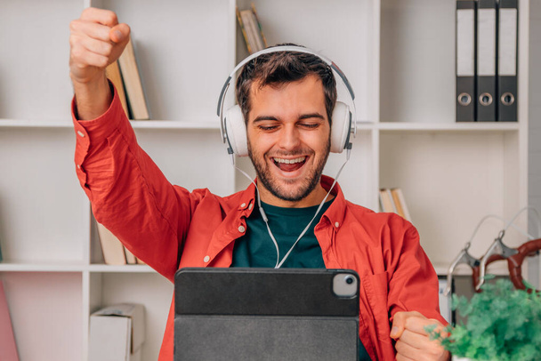 άνθρωπος στο σπίτι με ακουστικά και φορητό υπολογιστή γιορτάζει την επιτυχία - Φωτογραφία, εικόνα