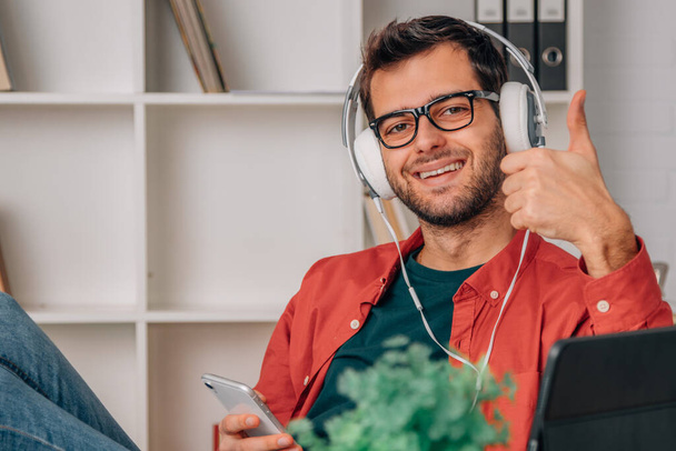 young man at home with mobile phone and headphones listening to music - Foto, Bild