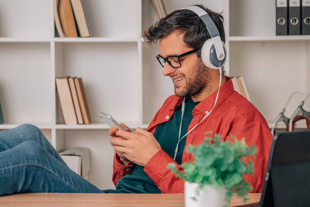 young man at home with mobile phone and headphones listening to music - Foto, Imagen