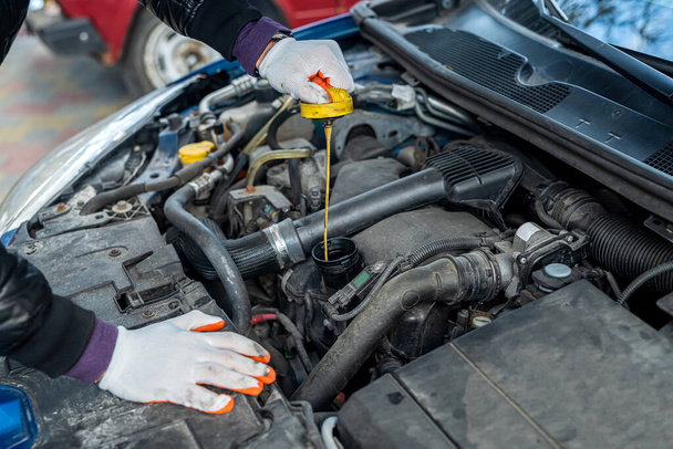 mecánico con las manos fuertes en guantes especiales repara un coche con una capucha abierta. concepto de reparación de coches - Foto, Imagen