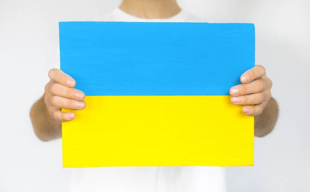 Guy with paper in the form of a yellow and blue flag of Ukraine on a white background. - Фото, изображение