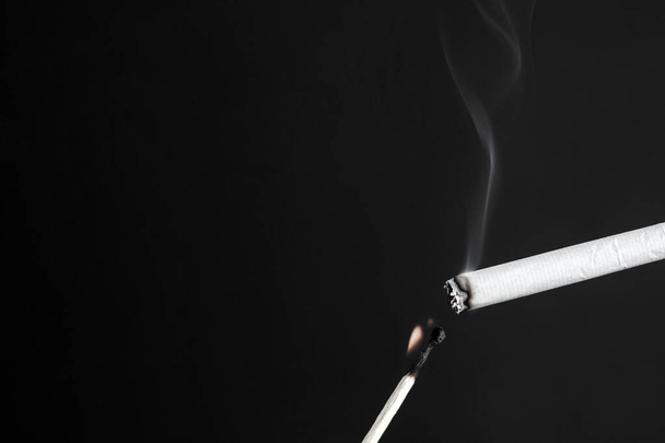 allumer une cigarette avec une allumette brûlante sur fond sombre. - Photo, image