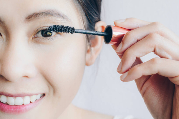 Close-up da jovem mulher asiática aplicando rímel preto em suas pestanas com pincel de maquiagem. O rímel é um cosmético comumente usado para realçar as pestanas. - Foto, Imagem