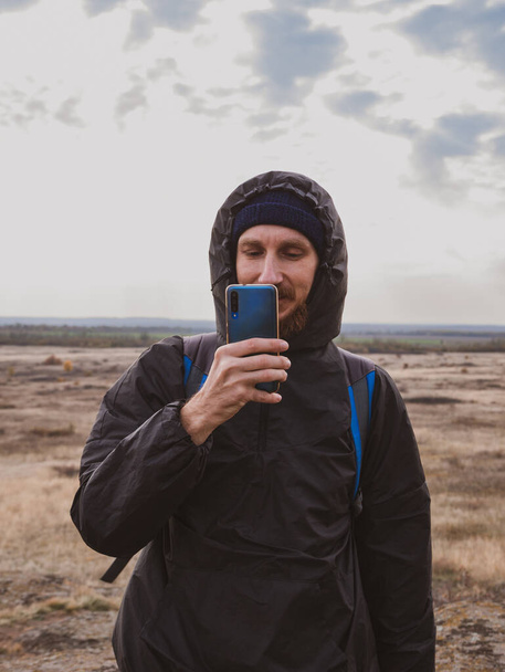 Podróżnik turysta fotograf człowiek z plecakiem smartfon wspinaczka szczyt górski robienie zdjęcia malowniczego krajobrazu zachmurzone niebo. Aktywny styl życia Solo Travel. Szlak turystyczny Backpacking extreme. - Zdjęcie, obraz