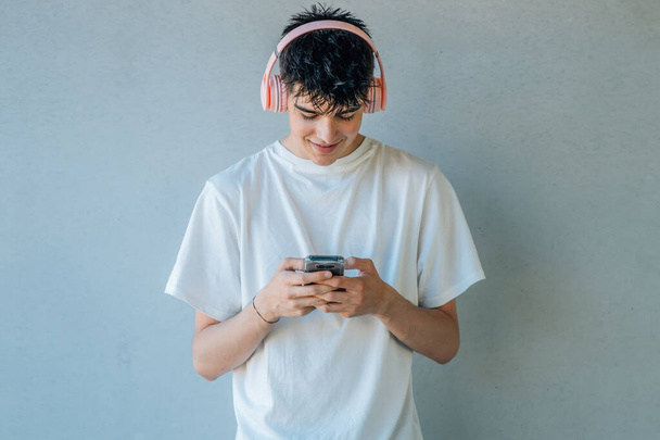 コピースペースで壁に隔離された音楽を聴く携帯電話やヘッドフォンを持つ10代の男の子 - 写真・画像