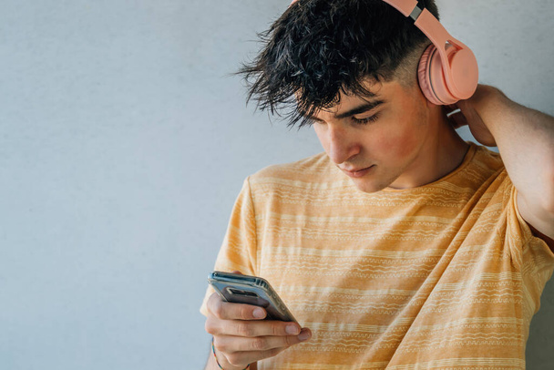 teenager s mobilním telefonem a sluchátky na šedém pozadí zdi - Fotografie, Obrázek