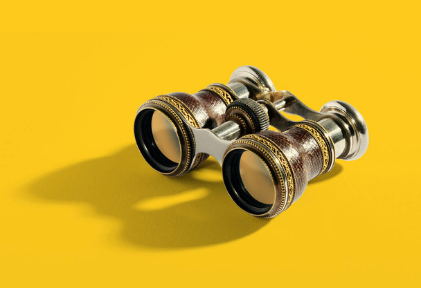 Pair of small vintage binoculars or opera glasses with a metal frame for magnifying objects at a distance on a yellow background with shadow detail - Photo, image