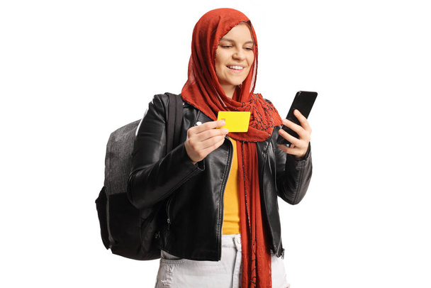 Female student with a hijab holding a smartphone and a credit card isolated on white background - Foto, afbeelding