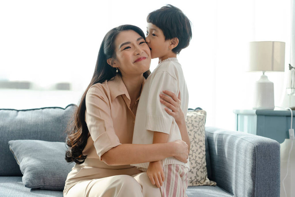 Happy Asian tender son kisses mother on mother's day during holiday celebration at home. - Photo, Image