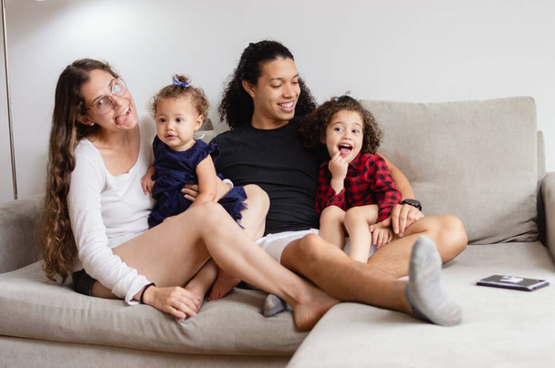 valkoihoinen onnellinen perhe istuu sohvalla tekemässä hauskoja kasvoja, äiti ja isä istuvat leikkimässä tyttäriensä kanssa olohuoneessa, elämäntapa käsite. - Valokuva, kuva