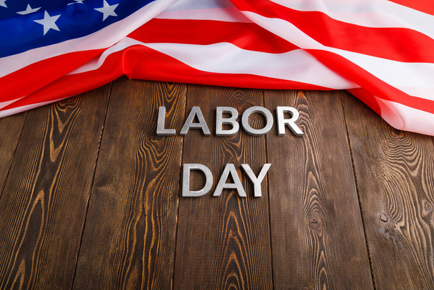 words labor day laid with silver metal letters on wooden surface with crumpled USA flag on left side - Foto, afbeelding