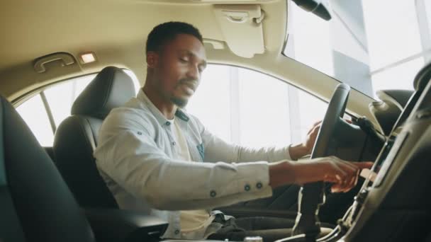 Ein Mann testet ein neues Auto. Seitenansicht eines fokussierten Afrikaners, der auf dem Fahrersitz sitzt und das Armaturenbrett zur Navigation nutzt. Mann drückt Touchscreen auf Multimedia-Panel im Auto, schaltet Radiosender. - Filmmaterial, Video