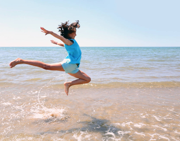 νεαρό αθλητικό κορίτσι κάνει άλματα δίπλα στη θάλασσα με τα πόδια ψηλά - Φωτογραφία, εικόνα