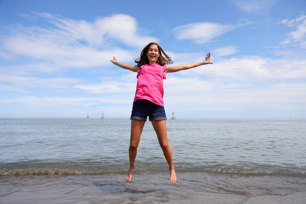 λεπτή νεαρή κοπέλα με κοντά παντελόνια στέκεται ένα πολύ υψηλό άλμα και είναι πολύ χαρούμενος το καλοκαίρι - Φωτογραφία, εικόνα