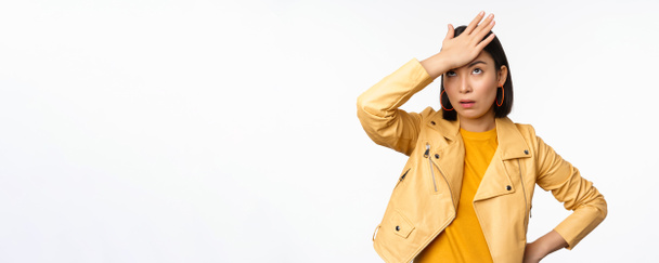 Vervelend en moe aziatisch meisje, klap voorhoofd, facepalm en eyeroll met lastige gezichtsuitdrukking, staan in casual kleding over witte studio achtergrond - Foto, afbeelding