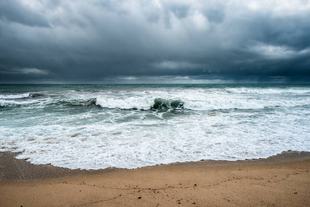 Rough seas crash onto the beach at Algajola in the Balagne region of Corsica with dark clouds and rain over the horizon - Photo, Image
