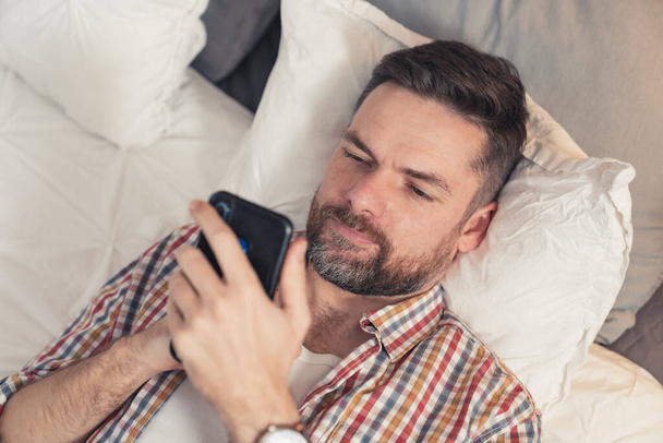 білий хлопець з повною бородою читає серйозну статтю онлайн, використовуючи свій новий чорний смартфон
 - Фото, зображення