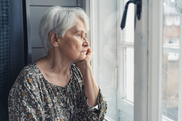 одинокий пенсионер сидит на кухне и печально смотрит в окно - Фото, изображение