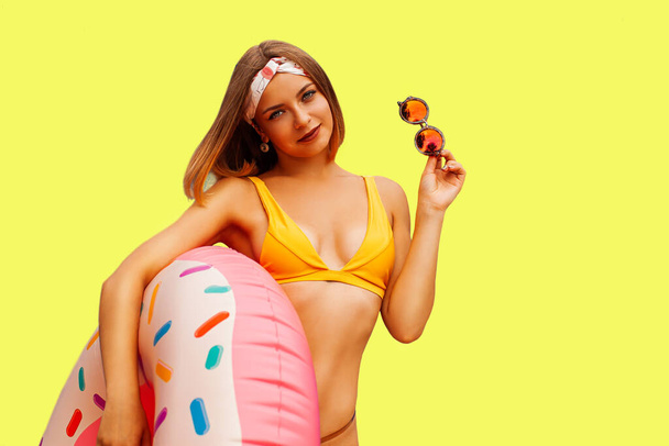 Щаслива сексуальна жінка тонке тіло в купальнику тримає рожеве надувне кільце ізольоване на яскраво-жовтому фоні стіни студії Літній готель басейн морський відпочинок концепція засмаги
 - Фото, зображення