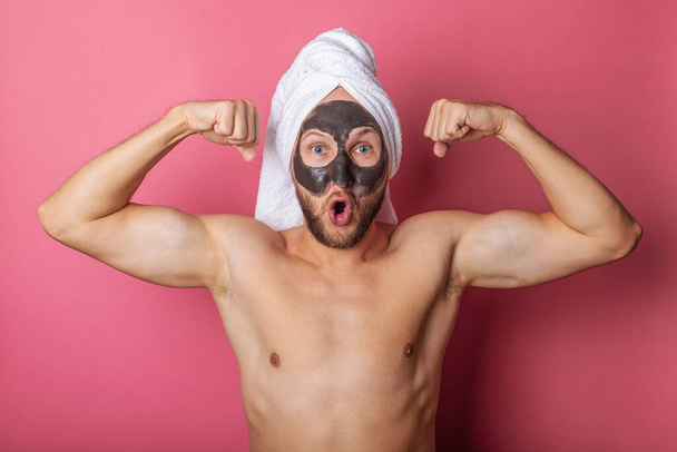 verraste naakte man met een cosmetisch masker op zijn gezicht, tonen spieren op een roze achtergrond. - Foto, afbeelding