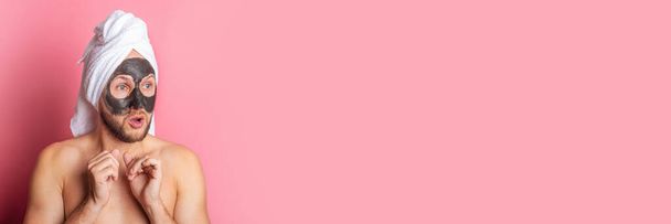 young man applies a moisturizing face mask, looks away in surprise on a pink background. Banner. - Photo, Image