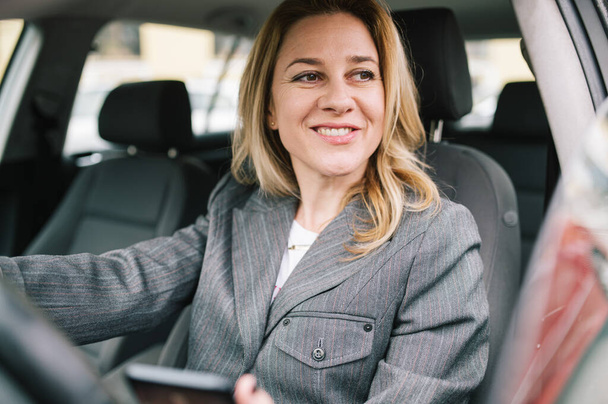 Молода бізнес-леді водить машину компанії і перевіряє свій телефон і дивиться у вікно
. - Фото, зображення