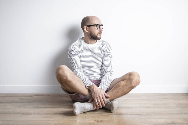 Young man in glasses sitting on the floor looking away  - Foto, Bild