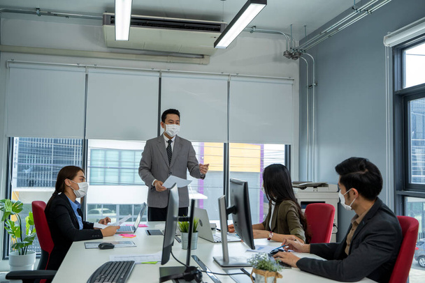 Uomini d'affari che indossano una maschera protettiva mentre lavorano insieme durante l'epidemia di coronavirus in ufficio. - Foto, immagini